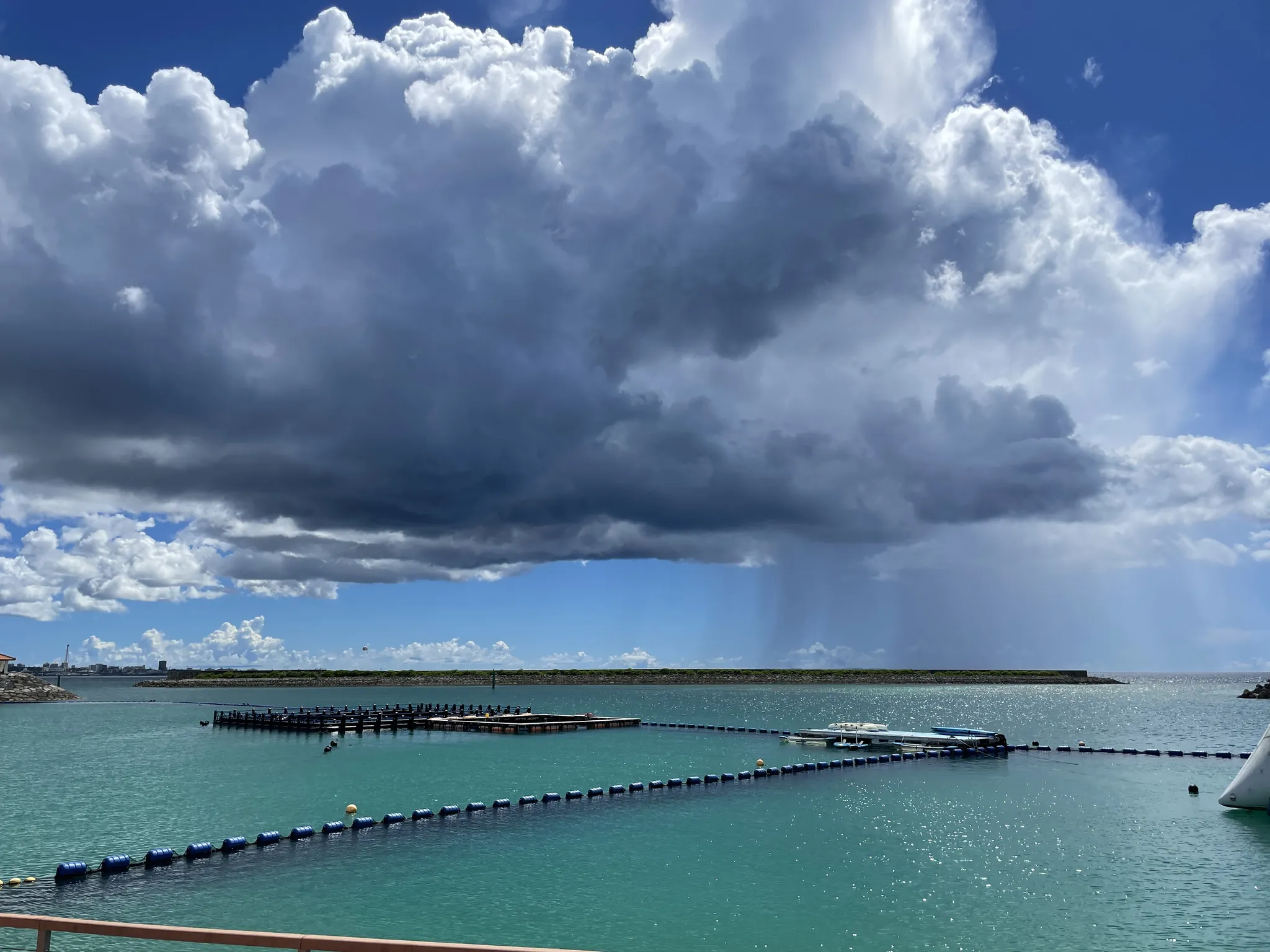 沖縄の夏の海。沖合にスコールの雨が降り、手前の海面にブイが並ぶ