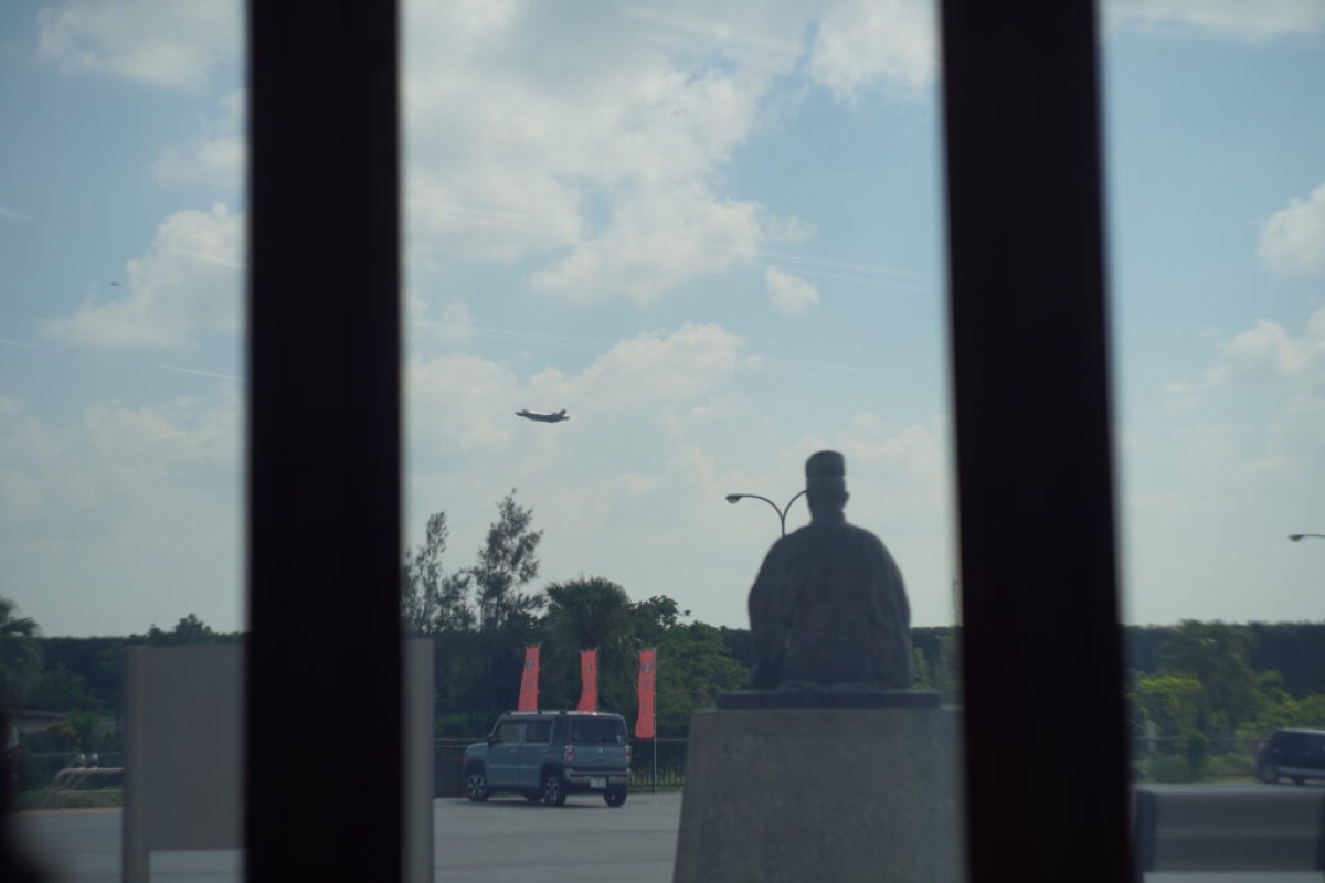 A fighter jet climbing out of Kadena Air Base seen past the Noguni Sokan statue