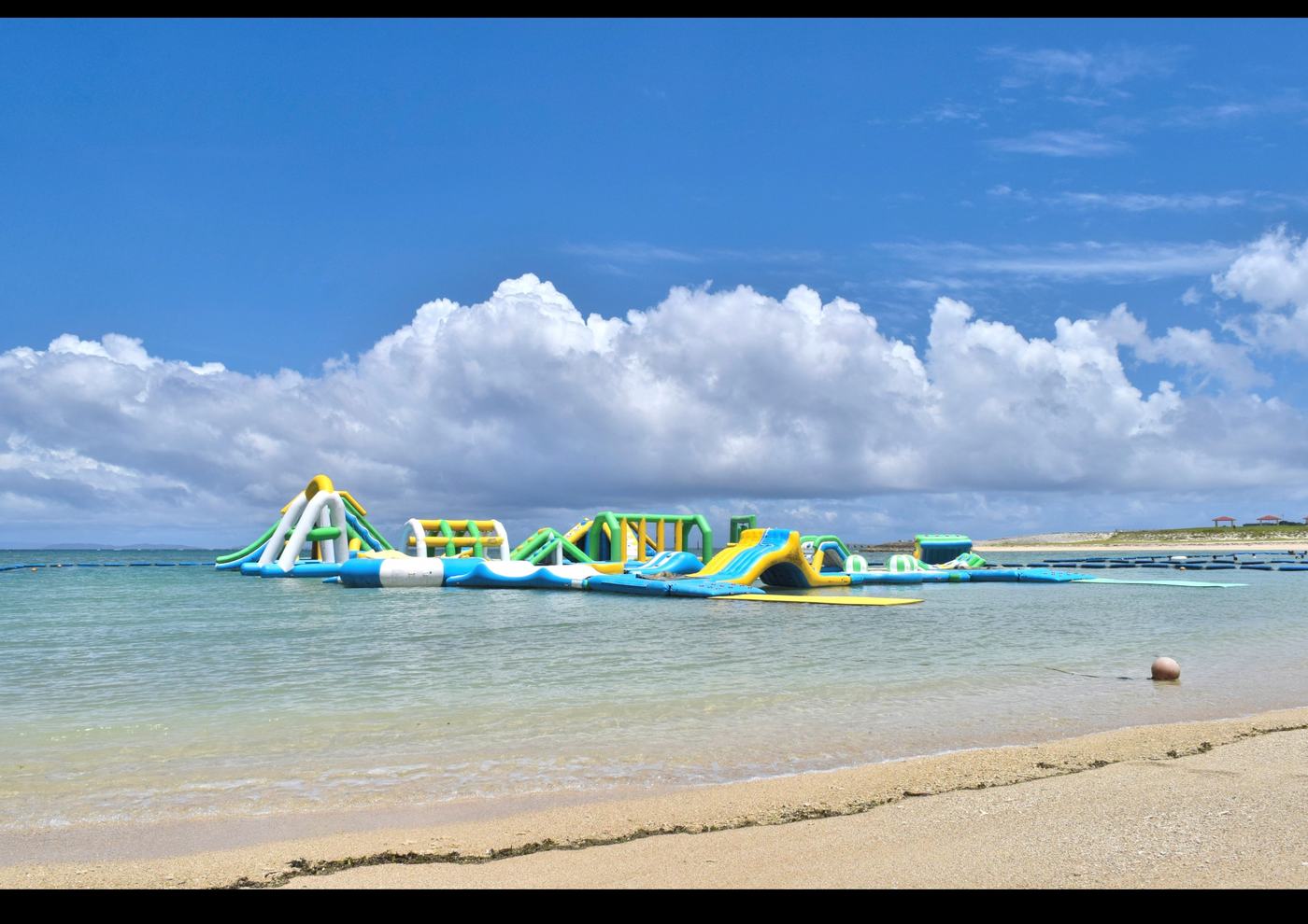 豊崎美らSUNビーチの浜と、沖に浮かぶ海上アスレチックと遊泳区域のブイ